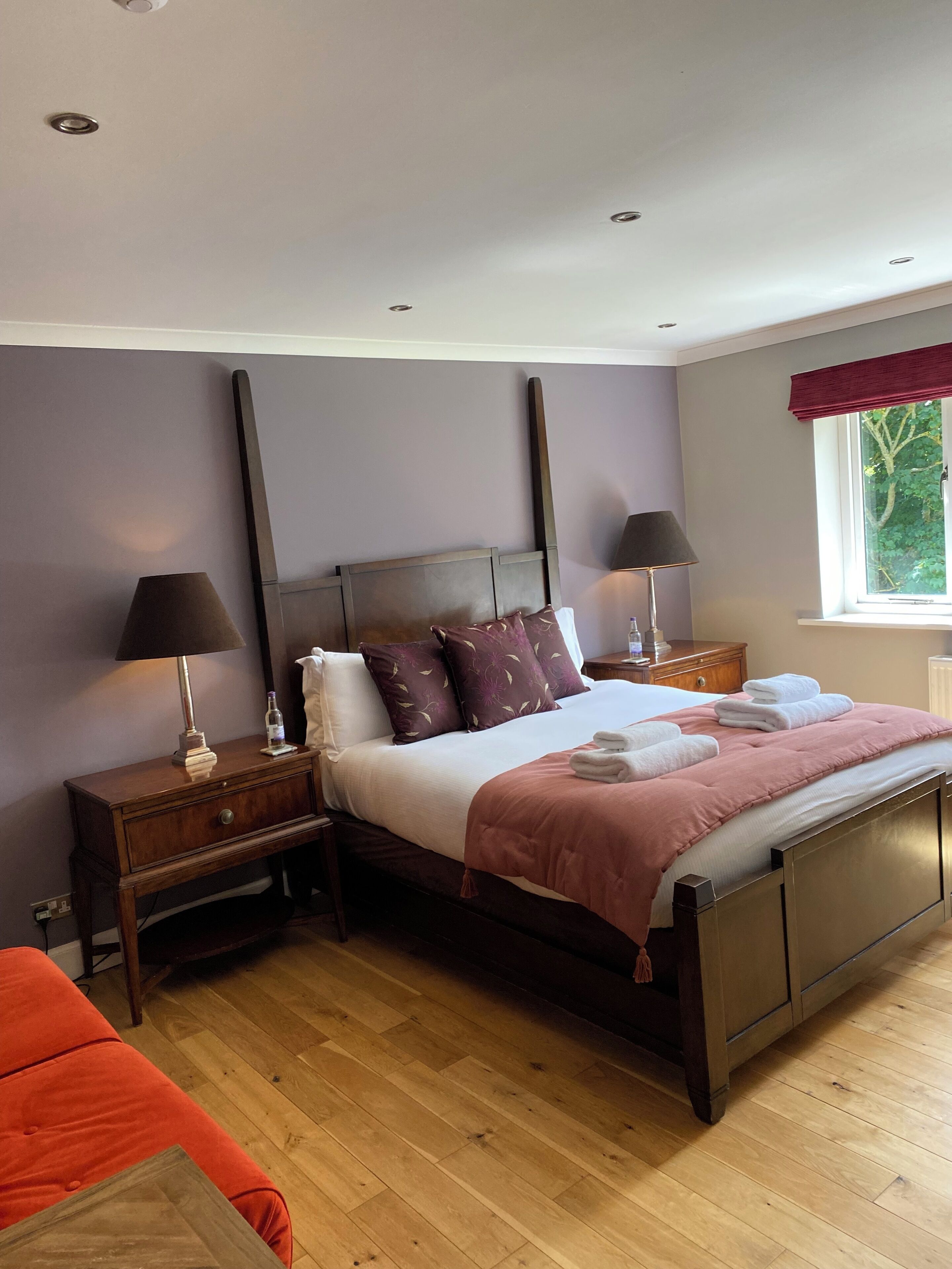 Quarto com cama, mesas de cabeceira, janela e uma cadeira vermelha.