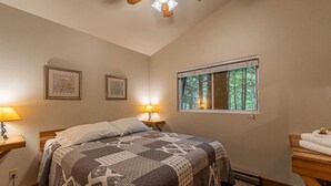 A bedroom with a bed, two bedside lamps, a window with a view of trees, and a ceiling fan.