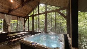 A hot tub in a wooden cabin with a view of a forest.