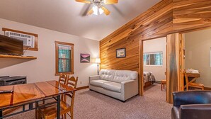 A room with a wooden wall, a white sofa, a dining table with chairs, and a ceiling fan.