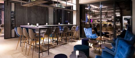 Uma área de estar moderna com uma mesa comprida e várias cadeiras, um bar e uma área de estar com cadeiras e pufes estofados em azul.