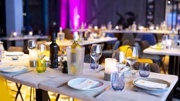 Ein Esstisch ist gedeckt mit Tellern, Gläsern und einer Flasche, in einem Restaurant mit modernem Ambiente und violetter Beleuchtung.