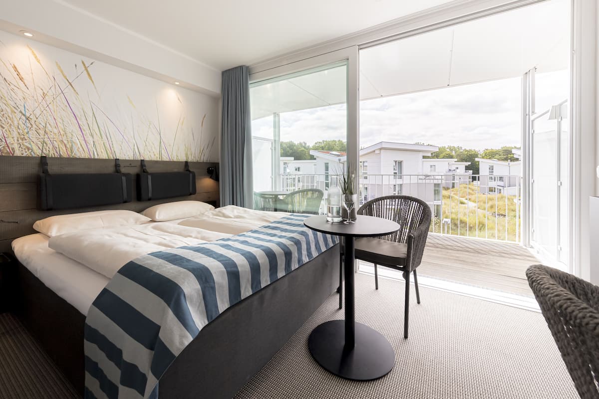 Een moderne hotelkamer met een groot bed, een ronde tafel en een stoel. Een groot raam biedt uitzicht op de stad.