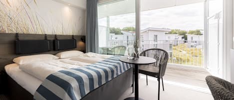 Quarto de hotel moderno com uma cama grande, uma mesa redonda e uma cadeira. Há uma janela ampla com vista para a cidade.