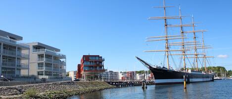 A tall ship docked at a marina with modern buildings in the background.