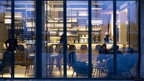 Un restaurante moderno con fachada de vidrio, asientos en el interior y una zona de bar visible a través de las ventanas.