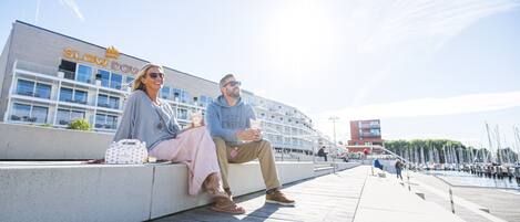 A couple sitting on a concrete ledge with a marina and boats in the background.