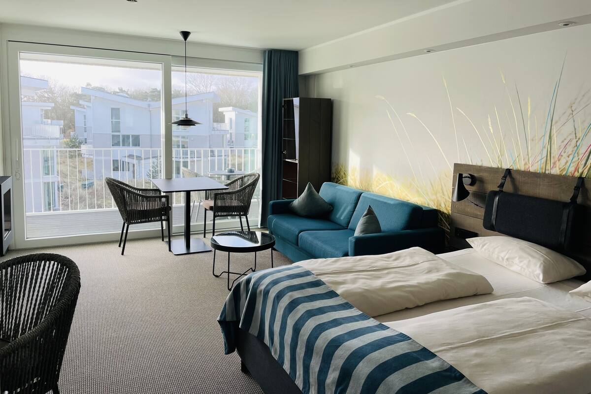 Een moderne hotelkamer met een groot balkon, een bank, een bed en een eettafel.