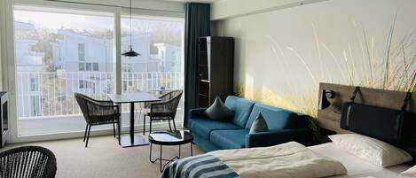 Una habitación de hotel moderna con un balcón grande, un sofá, una cama y una mesa de comedor.