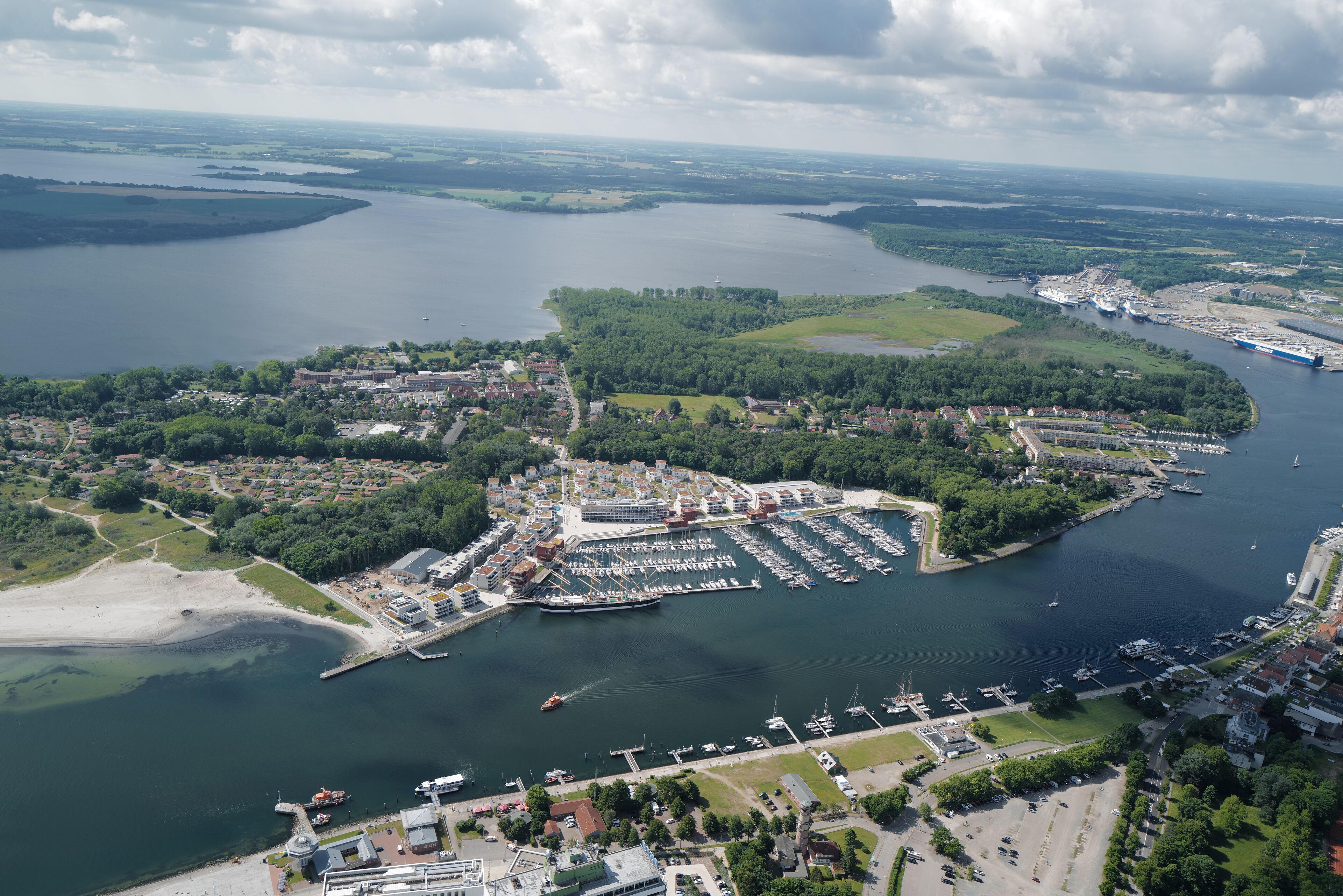 Vue aérienne d’une ville côtière avec un port de plaisance, des zones résidentielles et un grand navire de croisière amarré.