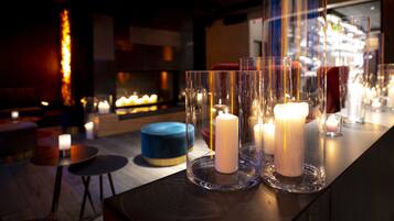 A bar area with candles in glass holders, a blue round seating, and a fireplace in the background.