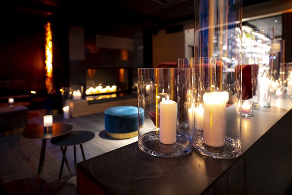 Zona de bar con velas en candelabros, un asiento circular azul y una chimenea al fondo.