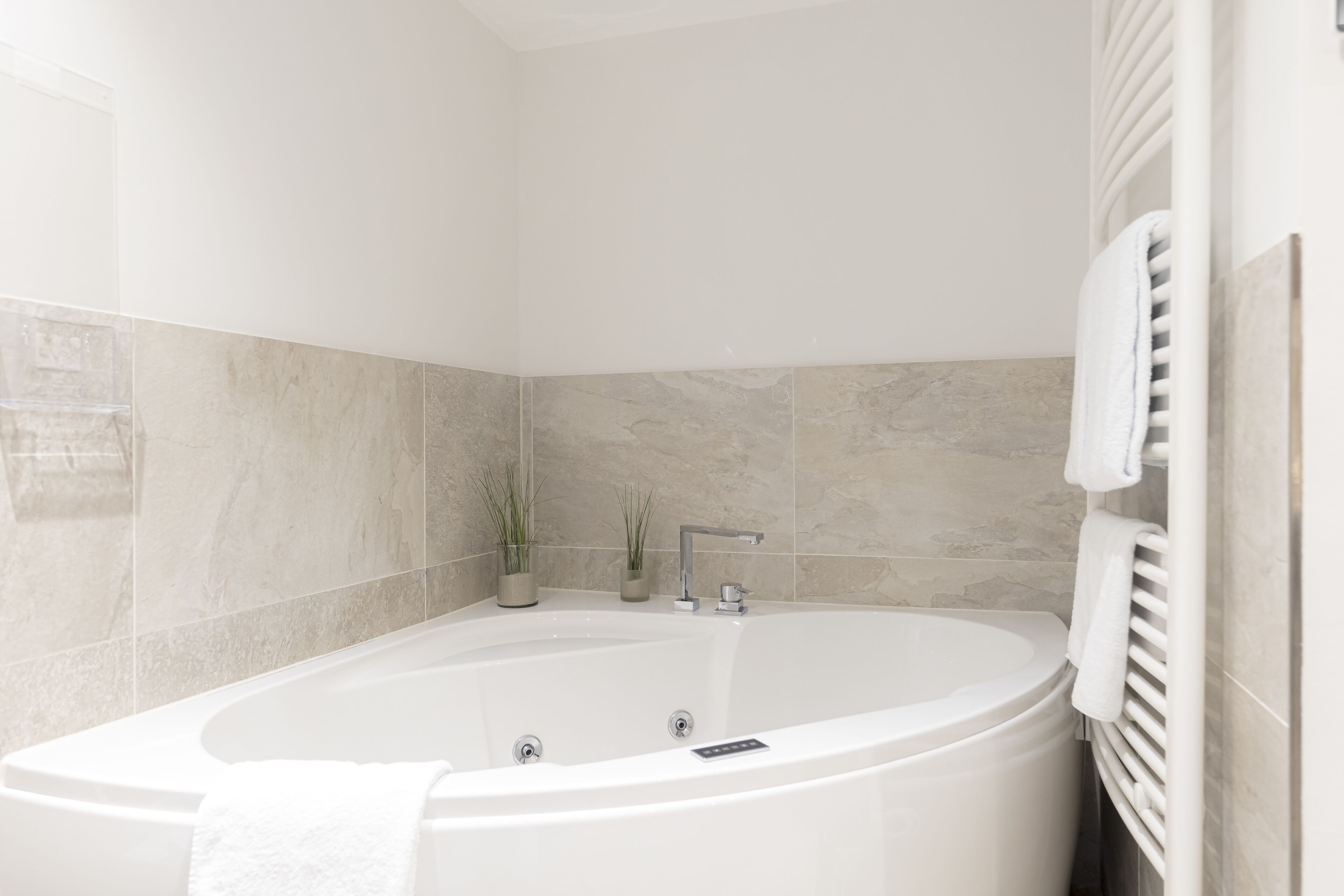 Un baño moderno con una bañera independiente, un perchero y dos plantas en macetas.