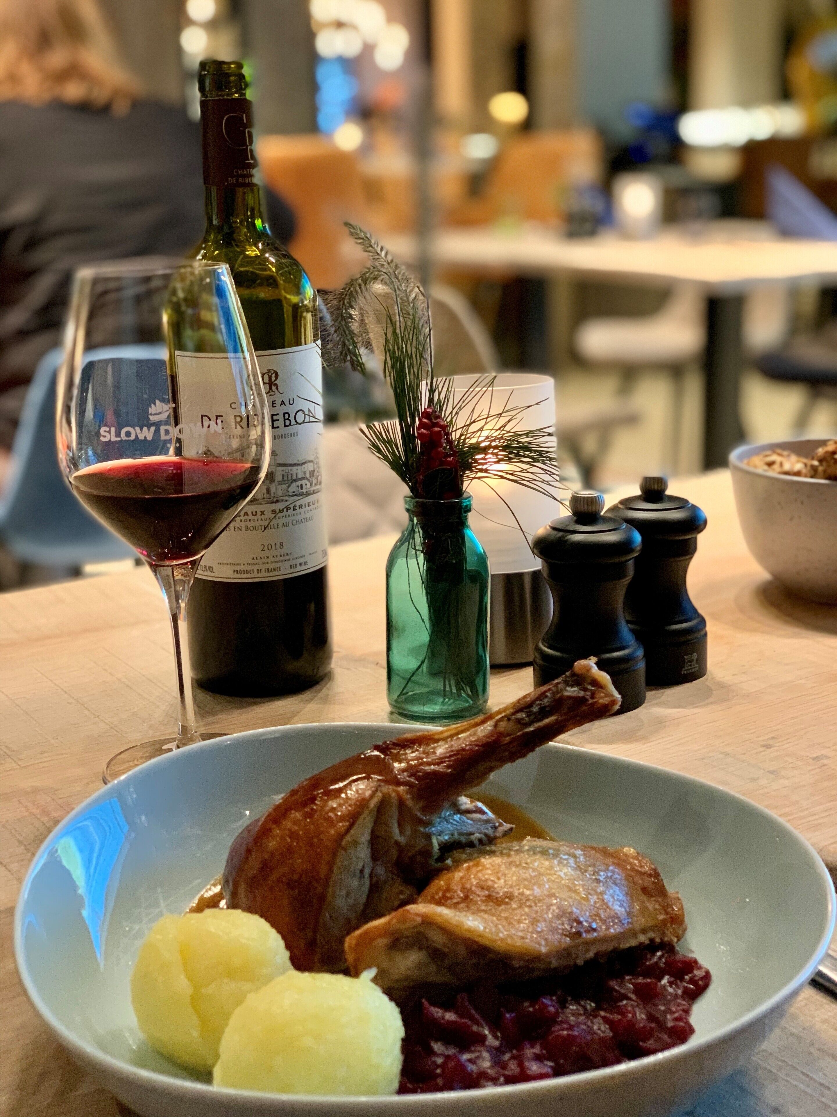 Una mesa de comedor con un pollo asado, patatas y una copa de vino tinto.