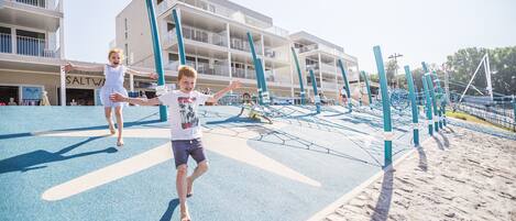 A playground with children playing, a building with balconies, and a sign that reads "SALTWATER".