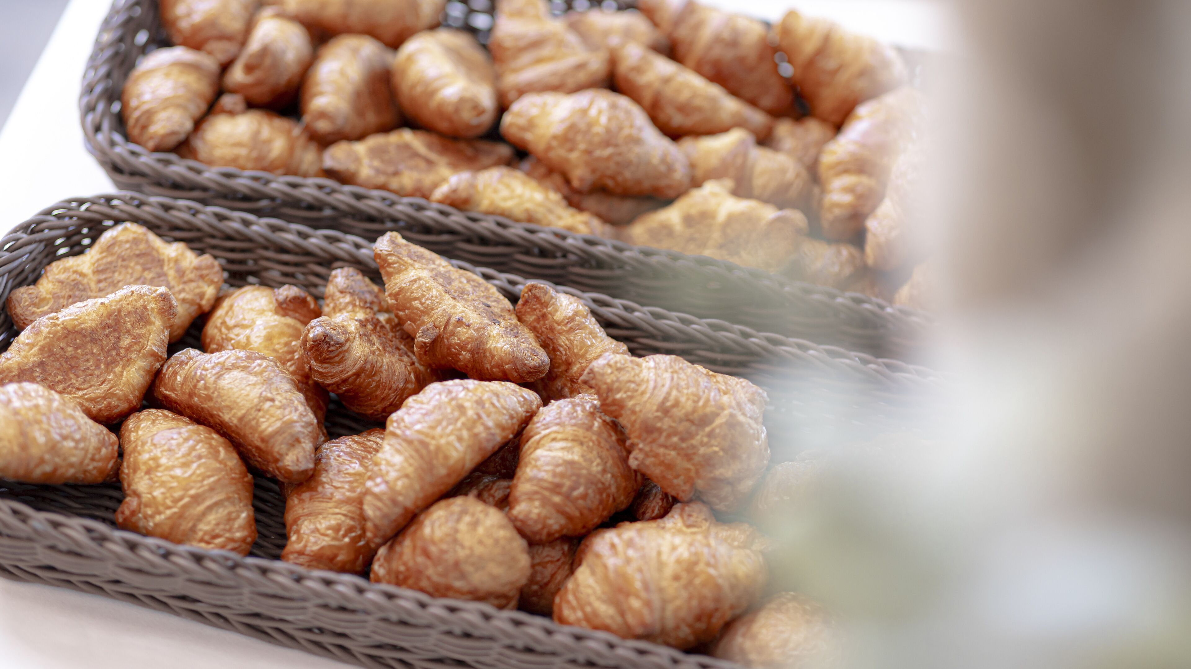 Una cesta rebosante de bollería dorada, probablemente croissants, dispuesta en cestas de mimbre.