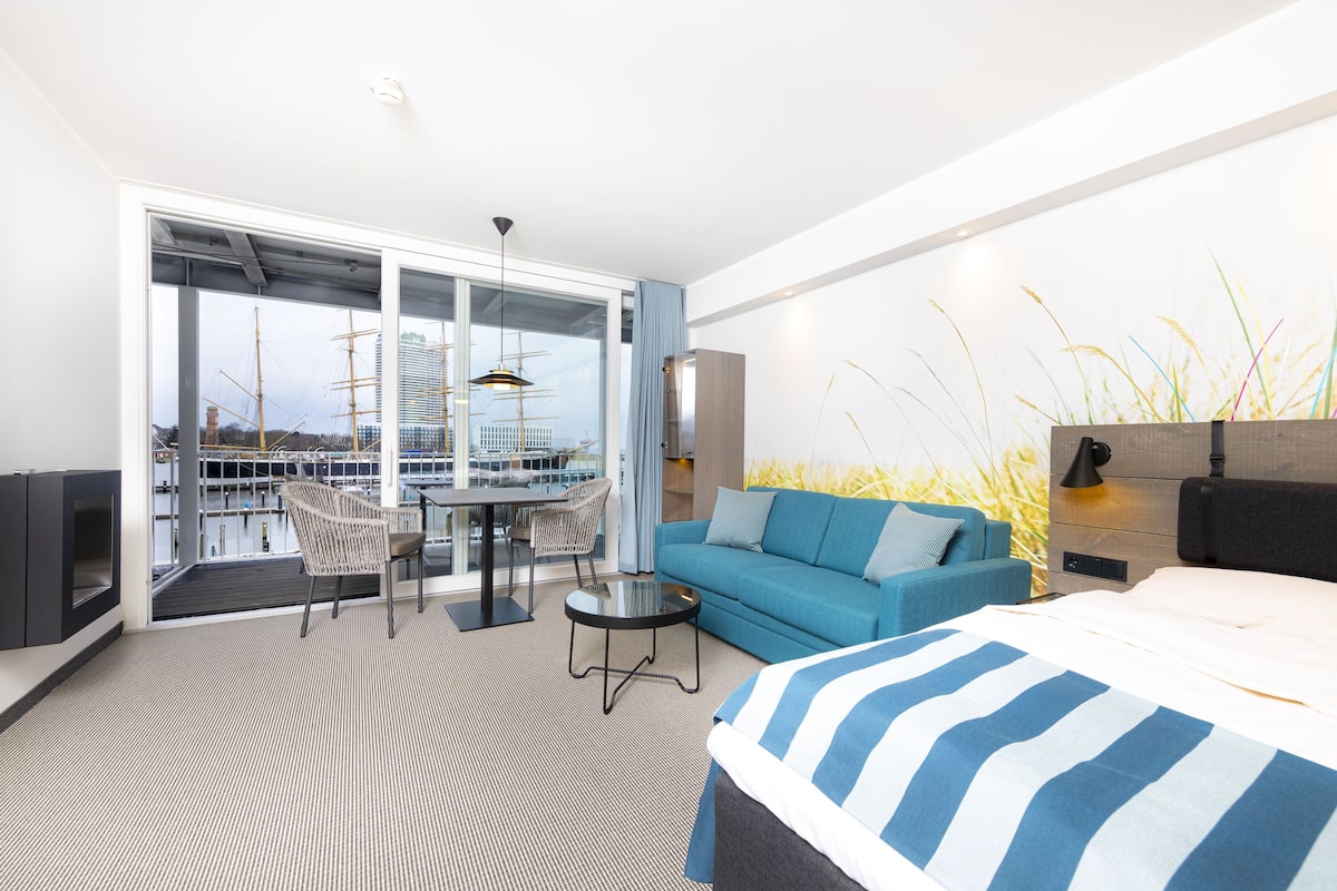 Een moderne hotelkamer met een groot bed, een slaapbank, een eettafel met stoelen en een balkon met uitzicht op de stad.