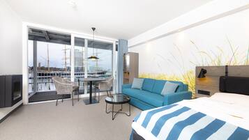 Een moderne hotelkamer met een groot bed, een slaapbank, een eettafel met stoelen en een balkon met uitzicht op de stad.