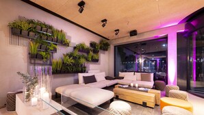 Una sala de estar moderna con sofá, reposapiés y una mesa de centro, una estantería de pared para plantas y un separador de vidrio.