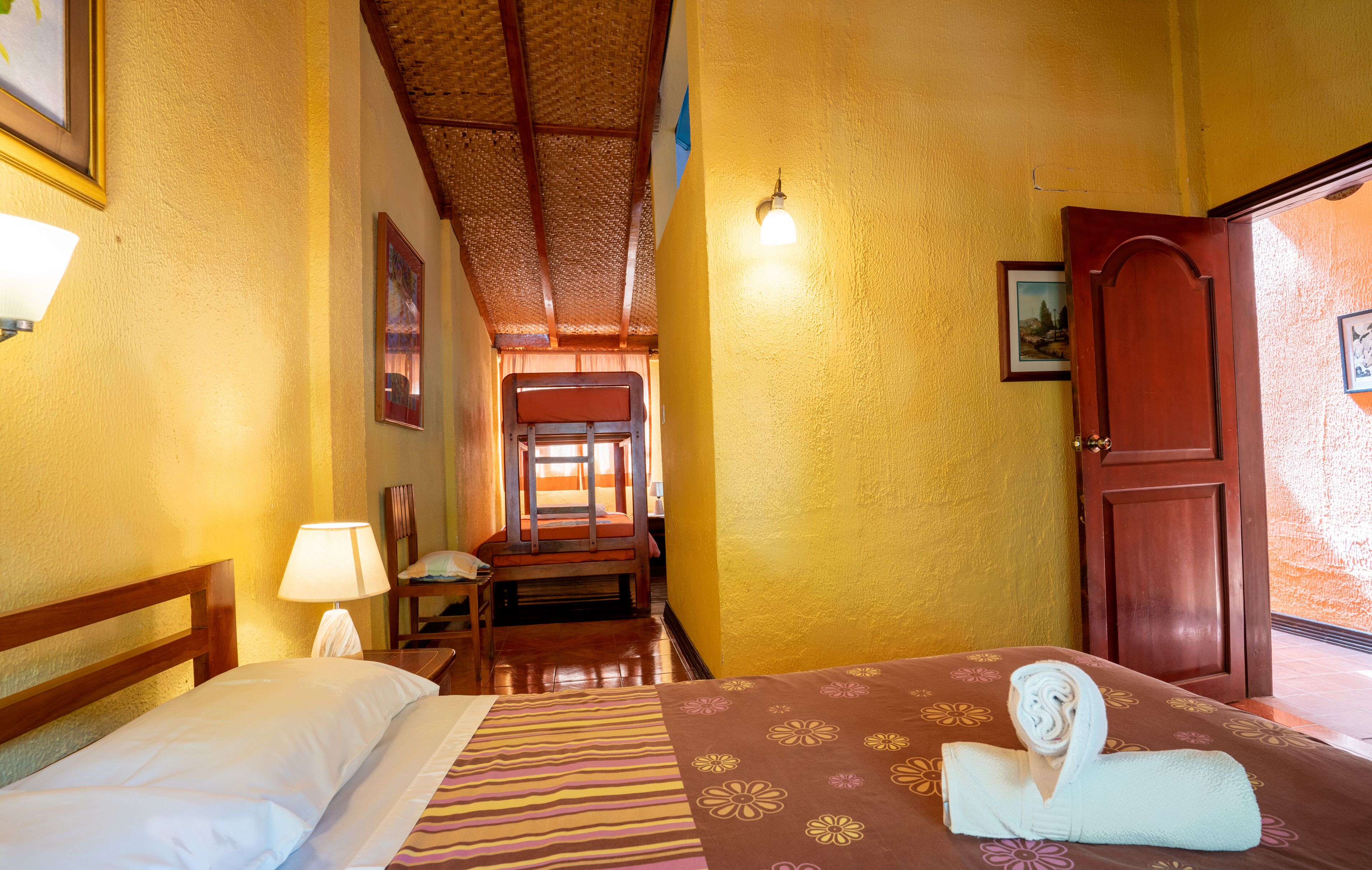 A hotel room with a bed, a chair, a lamp, and a door.
