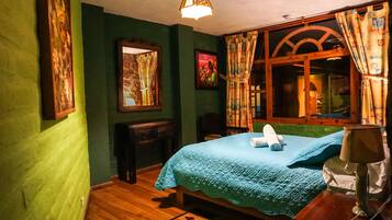 A room with a bed, a wooden nightstand, a desk, and a window with curtains.