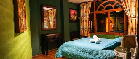 A room with a bed, a wooden nightstand, a desk, and a window with curtains.