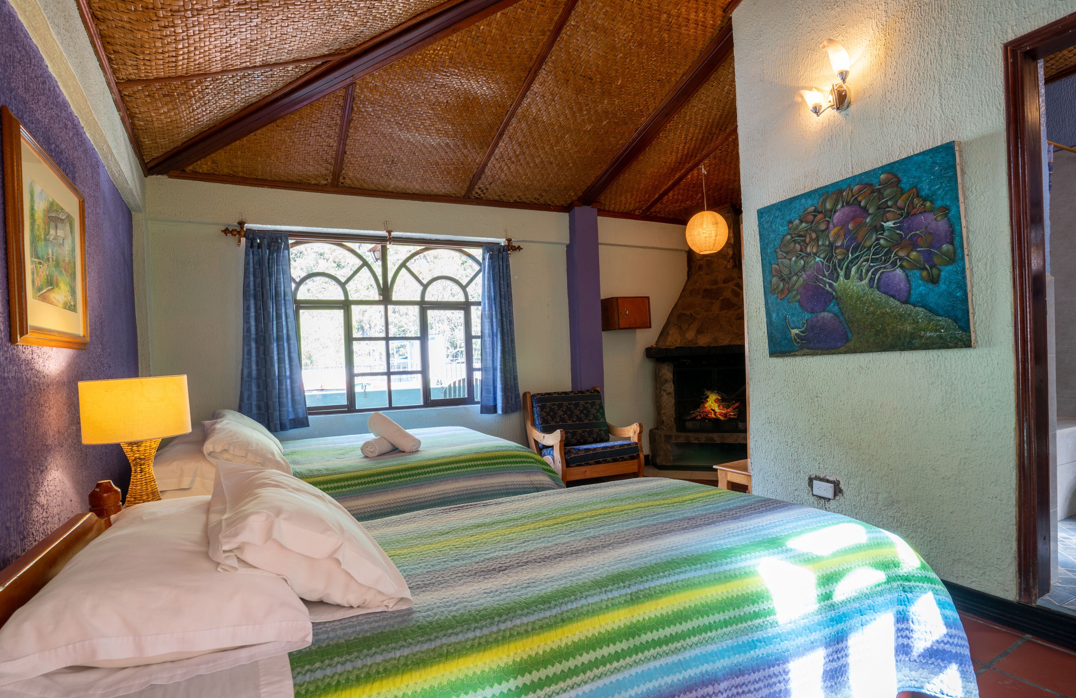 A room with a large bed, a chair, a fireplace, and a window with curtains.
