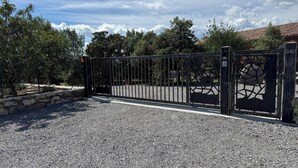 A gated driveway leading to a building with a stone wall and trees. - Villa L'Olivier with Private Pool and Spa in South Ardèche (Joyeuse)
