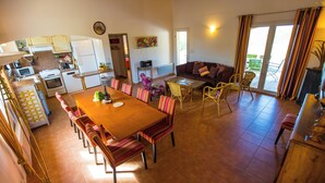 A spacious living area with a dining table, multiple chairs, a sofa, and a kitchen in the background. - Villa L'Olivier with Private Pool and Spa in South Ardèche (Joyeuse)