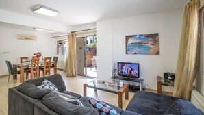 Ett vardagsrum med en soffa, ett soffbord, en tv och en matplats med stolar och ett bord.