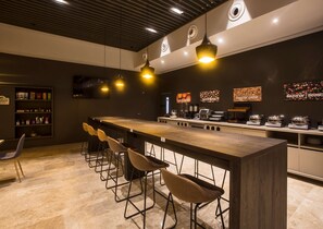 Un espace bar moderne doté d’un long comptoir, de nombreux tabourets et d’un éclairage suspendu.