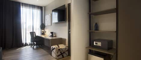 Una habitación de hotel moderna con suelo de madera, un escritorio con silla, un televisor de pantalla plana y estanterías empotradas con microondas.