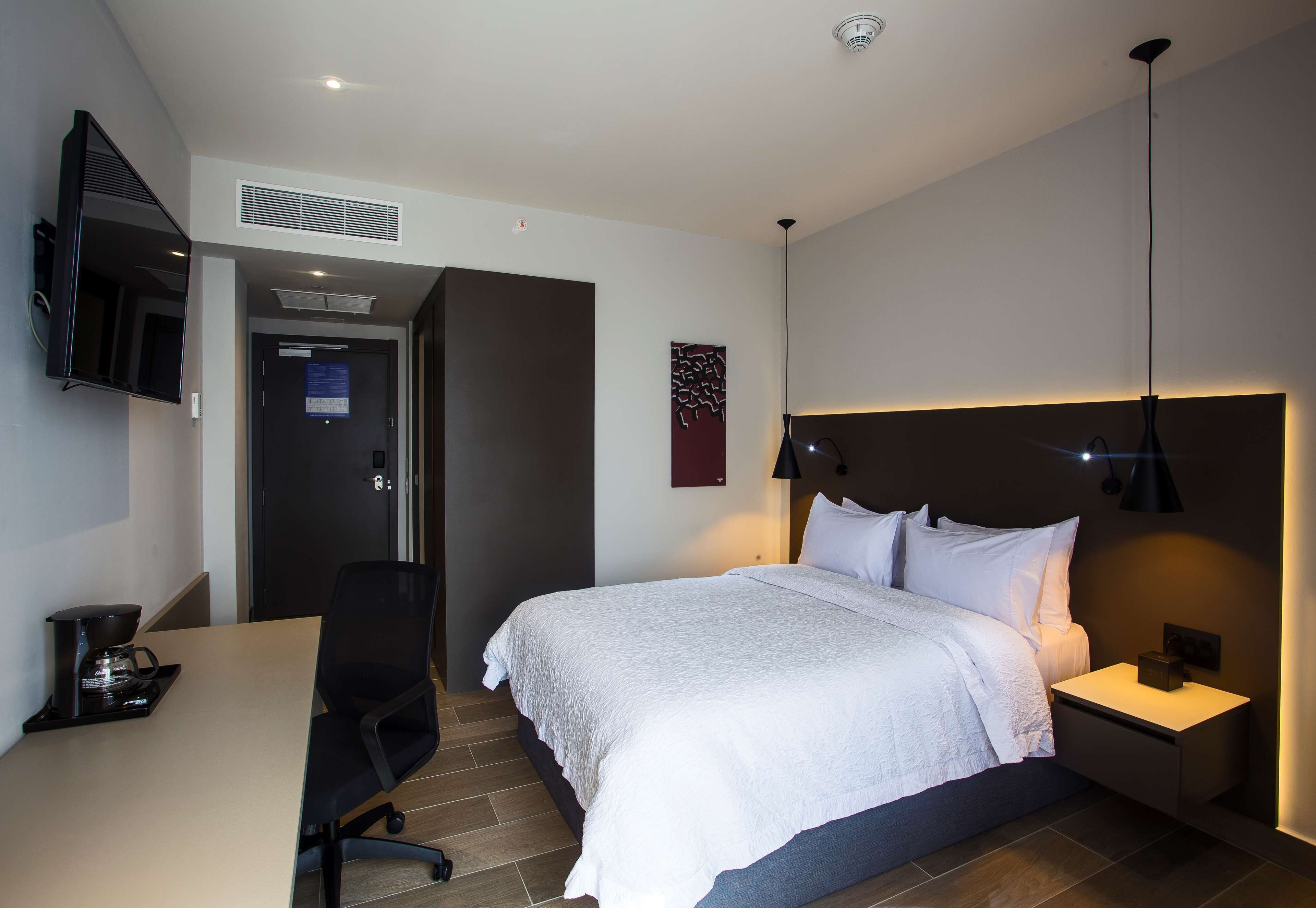 Una moderna camera d'albergo con un letto, un comodino, una lampada e una scrivania con una macchina per il caffè.