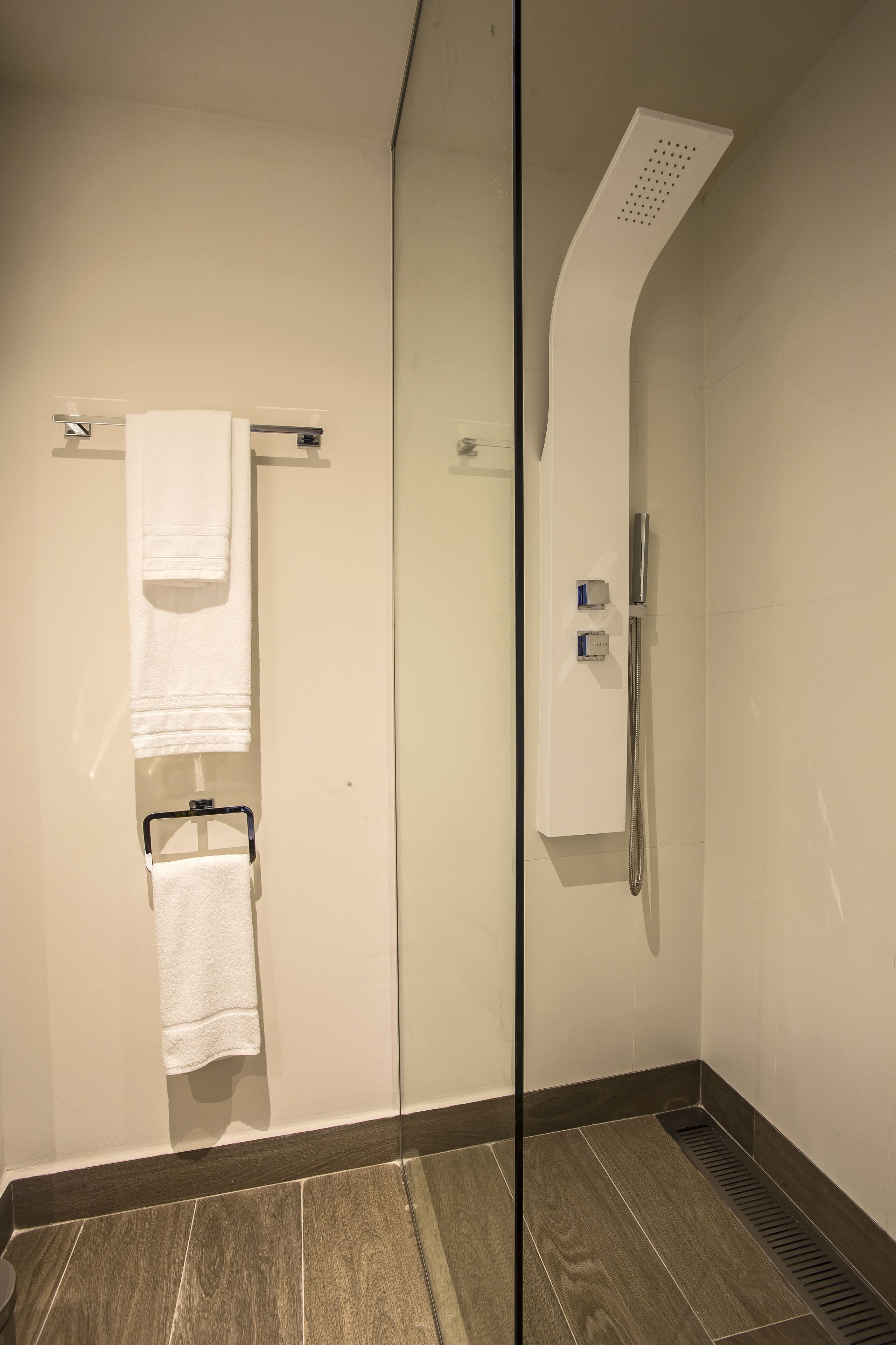 Un baño moderno con cabina de ducha de vidrio, un perchero con dos toallas y un calentador incorporado.