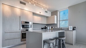 A modern kitchen with grey cabinetry, a central island with stools, built-in appliances, and a window providing natural light. - Relaxing Getaway with Intracoastal Views (Hollywood)