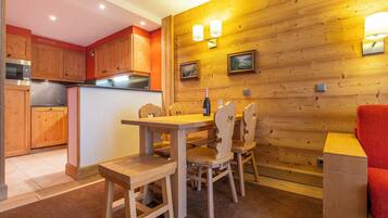 Un intérieur en bois comprenant une table et des chaises, un coin cuisine avec des meubles en bois et un éclairage fixé au mur.