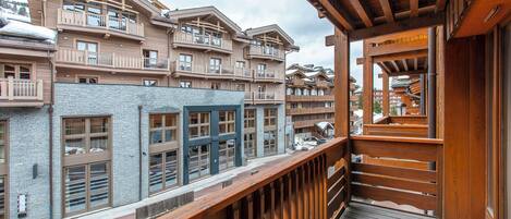 A wooden balcony with a view of multi-story buildings, featuring balconies and large windows.