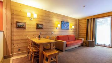 A cozy room with a wooden wall, a red sofa, a wooden table with chairs, and a bottle of champagne.
