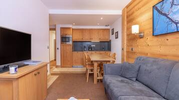 A compact living space with a flat-screen TV, wooden furniture, a sofa, and a kitchen area.