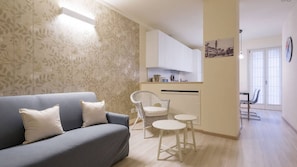 A living room with a grey sofa and white cushions, a wicker chair, and a small white table.