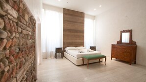 A bedroom with a stone wall, a wooden headboard, a bed with a green bench, a dresser, and a nightstand. - Mary House (Verona)
