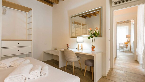 A hotel room with a bed, a desk, a chair, a mirror, and a bathroom visible through an open door.