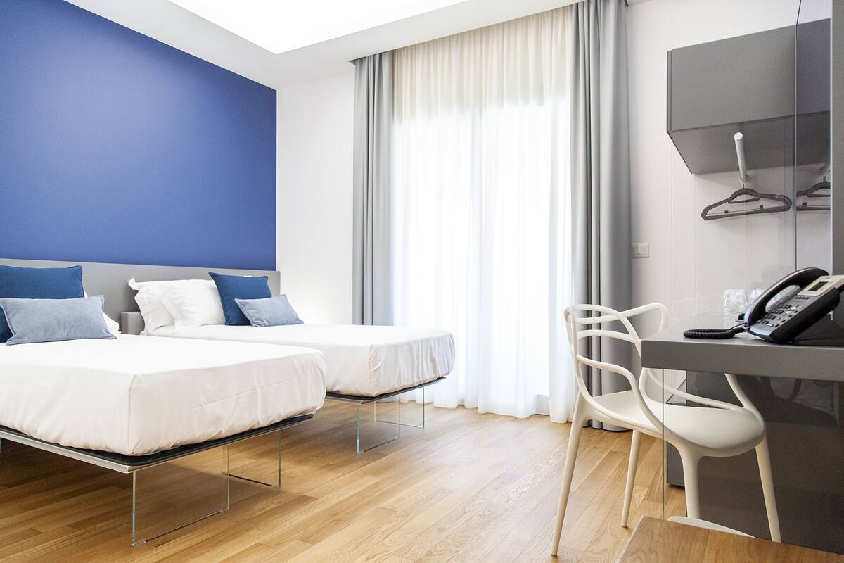 Une chambre d’hôtel avec deux lits, un bureau avec un téléphone et une chaise.