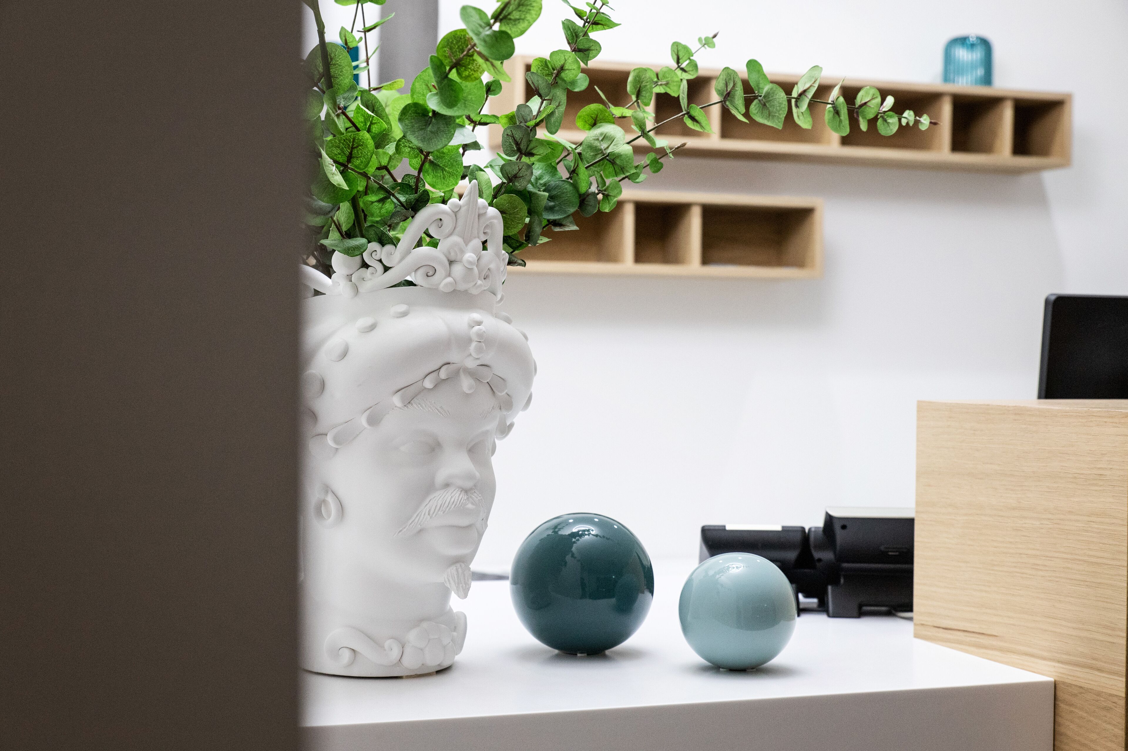 A white ceramic vase with a floral design, two spherical objects, and a black printer on a white surface.