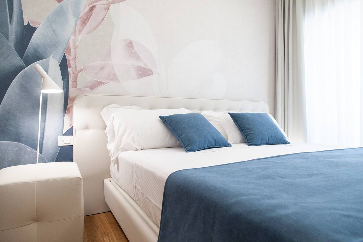 Une chambre moderne avec un lit, une tête de lit blanche et un mur d’accent bleu.