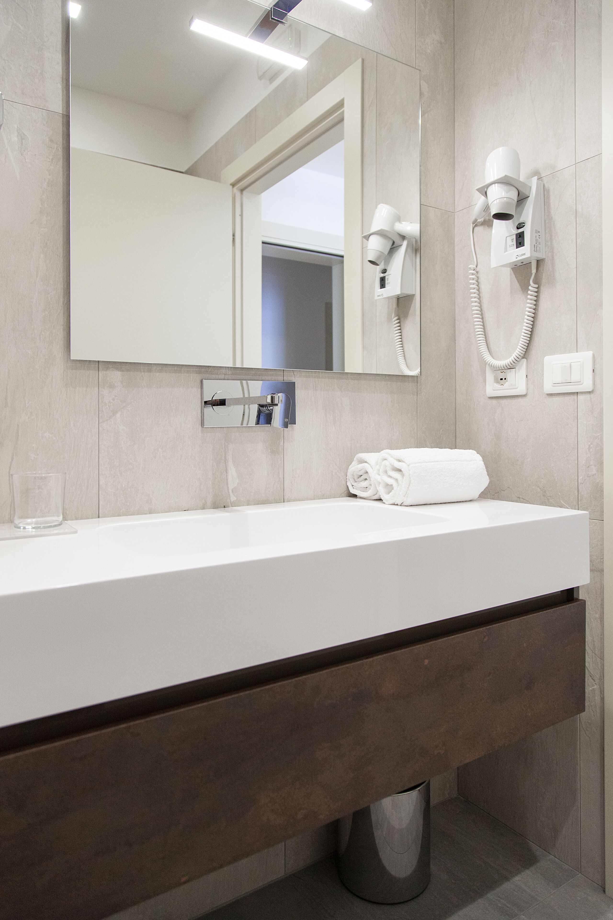 A modern bathroom with a white sink, a towel, a hairdryer, and a mirror.
