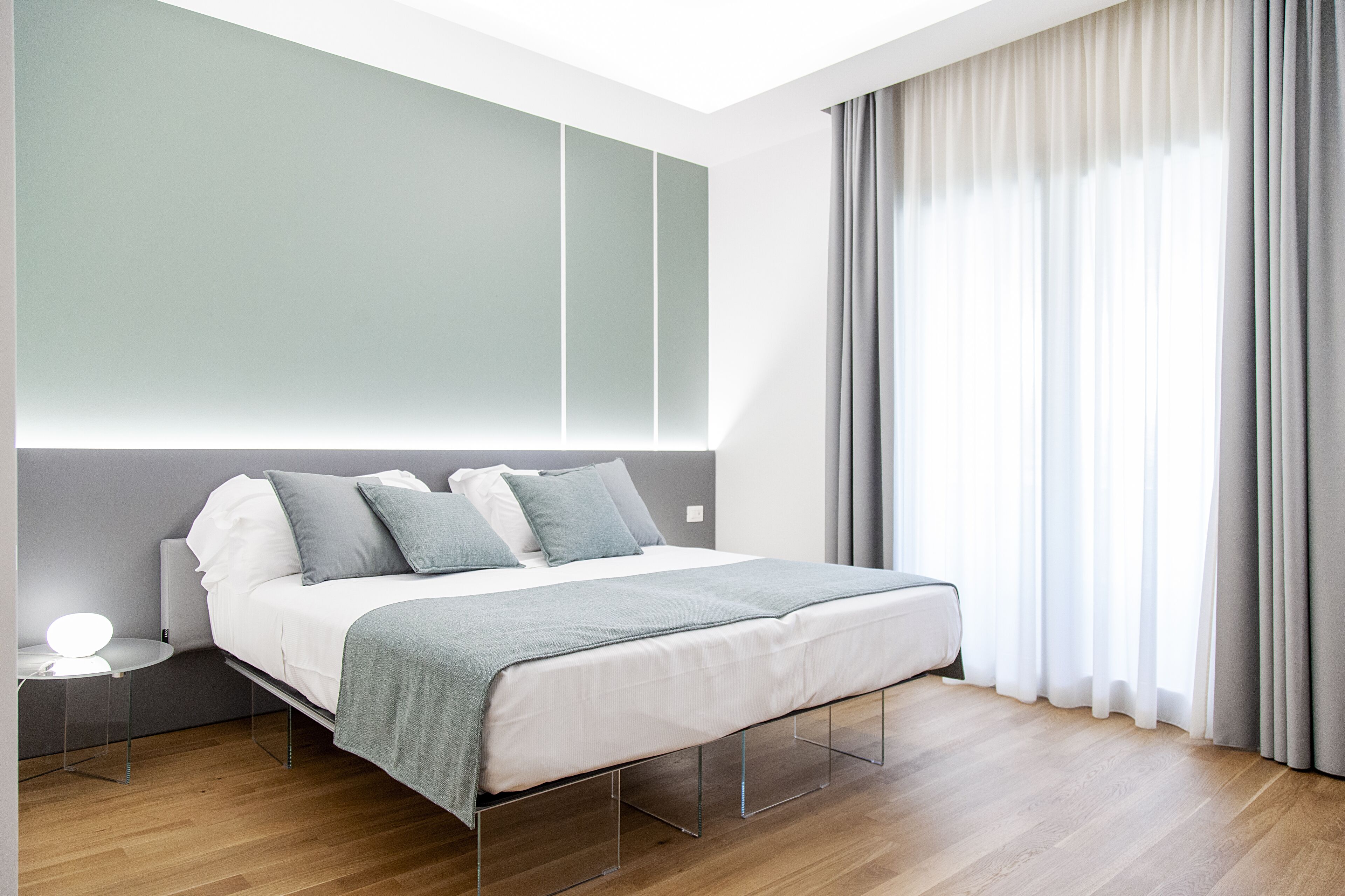 A modern bedroom with a bed, bedside table, and a large window with curtains.