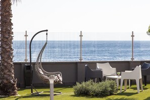 Un patio con una silla colgante, sillas blancas y una mesa con vista al océano.