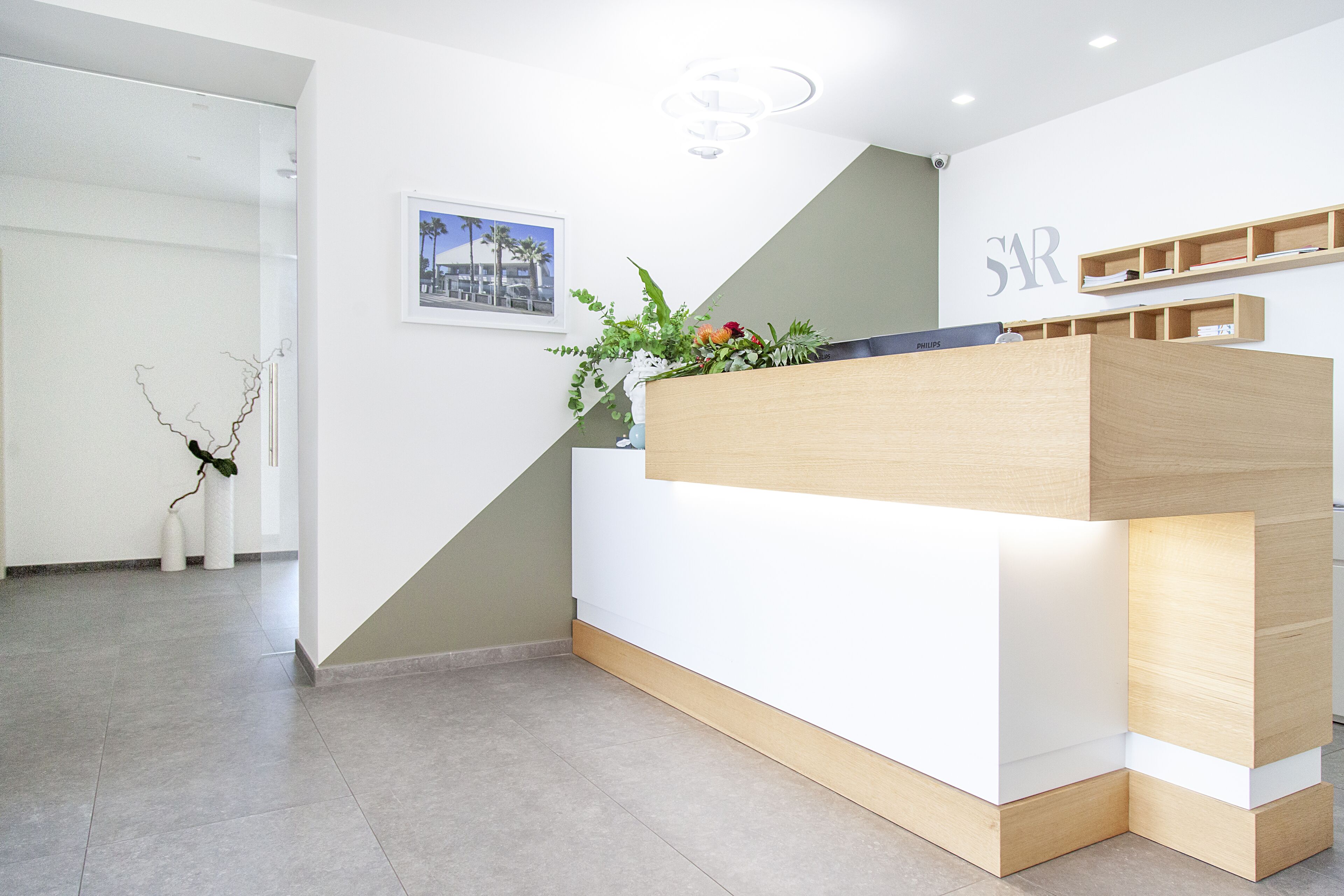 A reception desk with a plant, a framed picture, and a 'SAR' sign on the wall.