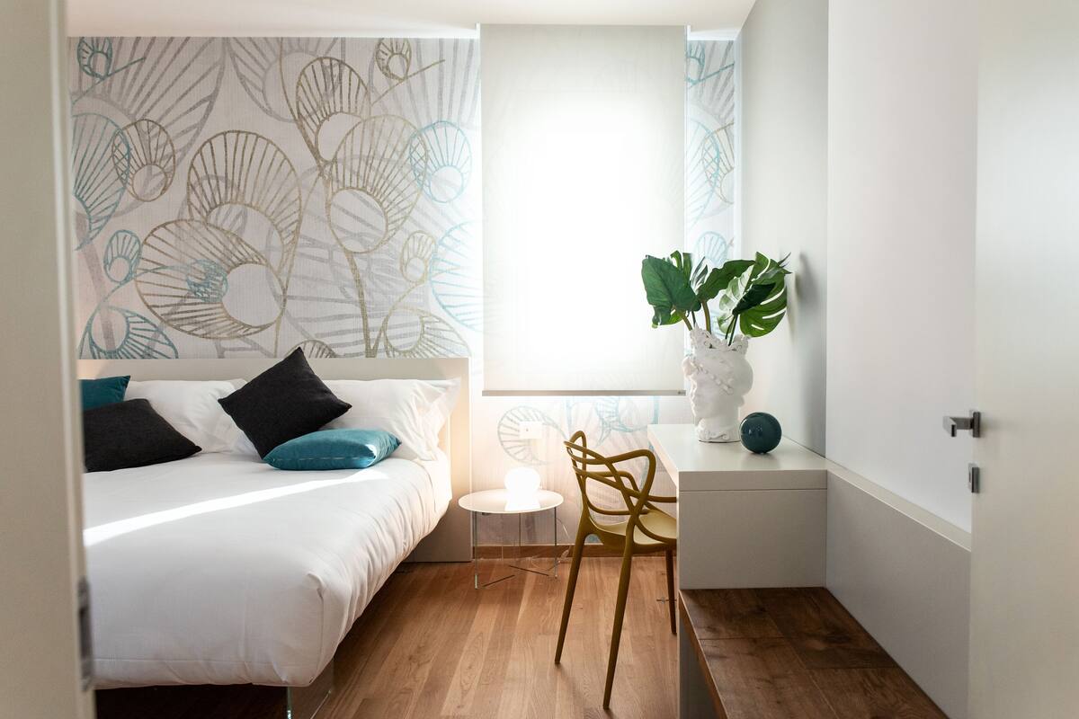 Une chambre à coucher avec un lit, une petite table, une chaise, une plante en pot et une fenêtre donnant sur un beau paysage.